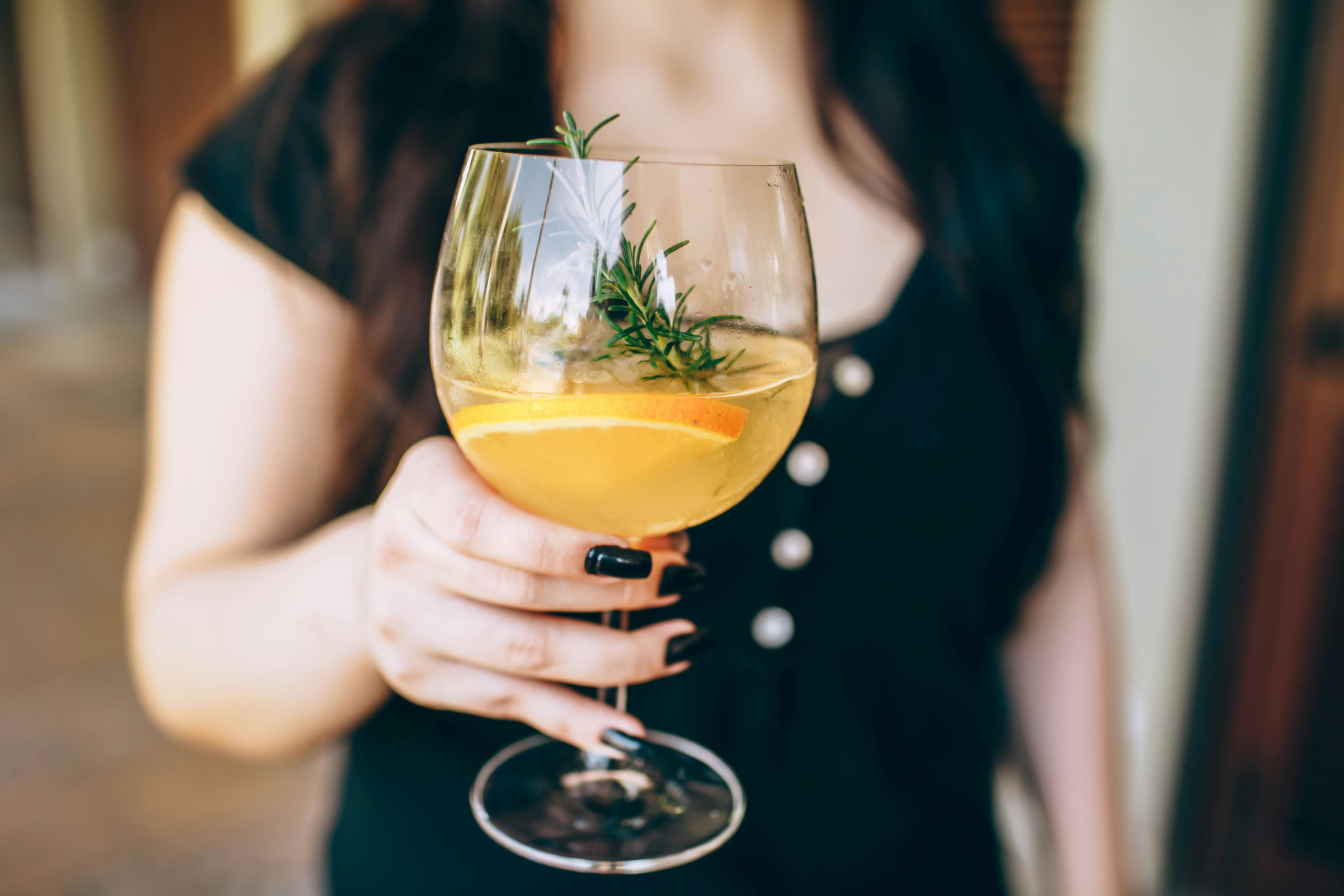 woman holding clear wine glass with yellow liquid